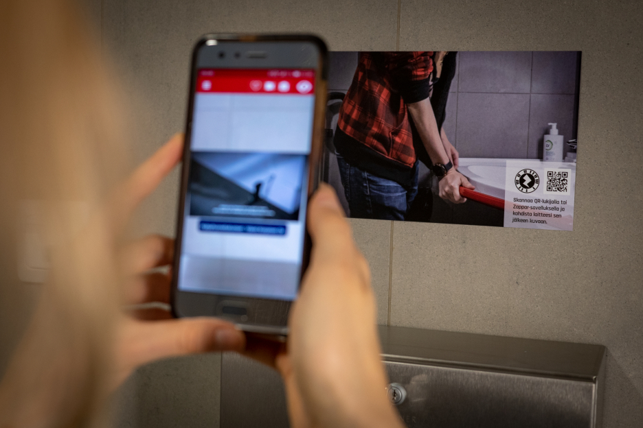 Woman points at a picture on the wall with a mobile phone