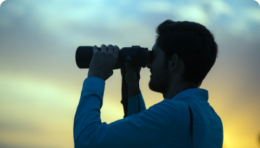 mies katsoo kiikareilla kaukaisuuteen